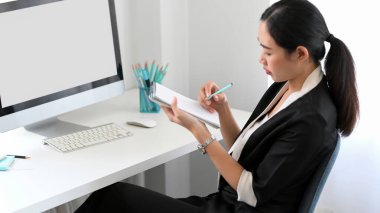 A professional female accountant taking a notes on notepad at her comfort office workplace.