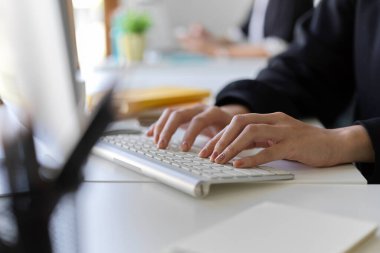 Cropped image of a worker working on pc computer, typing on keyboard, managing her online assignment in the office.