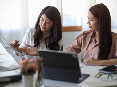 Female manager coaching, training and briefing work assignment to her financial assistant at the office. 