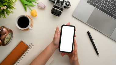 Female freelance photographer using her smartphone on her working desk. mobile phone blank screen.