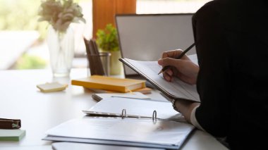 Close-up, a female assistant or secretary taking notes on the financial report at her office desk.
