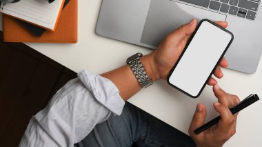 Male freelancer is using a smartphone at his office desk. phone blank screen. Top view, close-up
