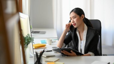 An Asian female entrepreneur is talking with her supplier on the phone. A businesswoman is calling her partner.