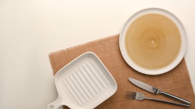 Flat lay, an empty plate with empty small white pan plate and silverware on placemat over white background.