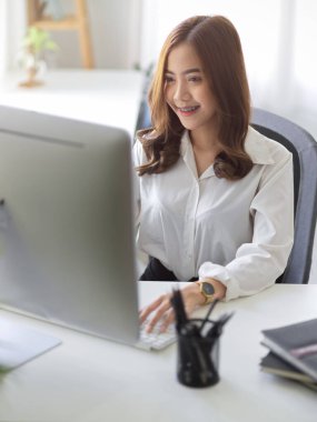 Güzel Asyalı genç bayan asyalı asistan ya da sekreter ofisindeki bilgisayarında çalışıyor..