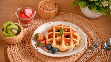 Taze dutlu bir tabak lezzetli waffle, bir fincan taze kivi, çilek ve tahıl gevreği..