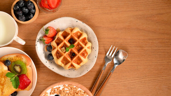 Концепция вкусной выпечки с вафлями, тостами, йогуртом и свежими ягодами на фоне деревянного стола.