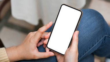 Rahat koltuklarda oturan ve akıllı telefonunu kullanan genç bir kadının yakın plan görüntüsü. Akıllı telefon boş ekran. İnternetten alışveriş, internette sörf, sosyal medya.