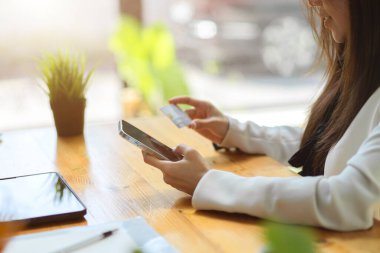 Yan görüş, akıllı telefon, kredi kartı ya da banka kartı tutan bir kadın işçi. çevrimiçi ödeme veya çevrimiçi alışveriş kavramı.