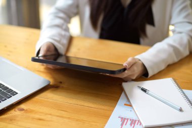 Yakın plan, kadın çalışan taşınabilir tablet bilgisayar kullanıyor, tablet ekrandan bazı bilgilere bakıyor, masanın üzerinde bir dokunmatik ped tutuyor..