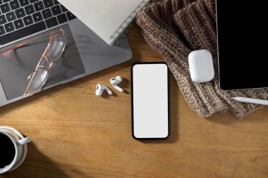 Dizüstü bilgisayarı, kulaklıkları, tableti, zımbırtısı ve ahşap masanın üzerinde akıllı telefon beyaz ekran modeli olan basit bir ofis masası. en üstteki görünüm