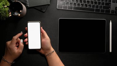 Modern siyah ofis masası üst görünümü kadın eli ile çalışma alanı üzerinde akıllı telefon boş ekran kullanın.