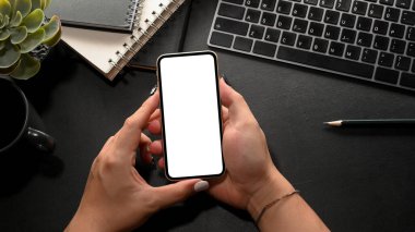 Yakın plan, hippi kadın elinde akıllı telefon boş ekran modeliyle modern siyah çalışma ortamı üzerinde duruyor..