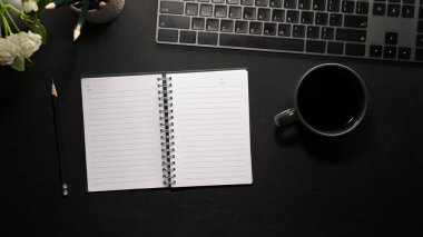 Modern ofis çalışma alanı üst görünümü boş defter sayfaları ve ofis malzemeleri siyah masa arkasında. Kırtasiye aksesuarları ofis masasında.