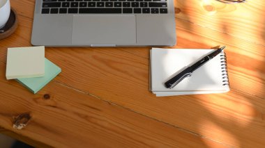 Laptop bilgisayarı, not defteri, kalem, yapışkan notlar ve kopyalama alanı olan basit ahşap ofis masası. en üstteki görünüm