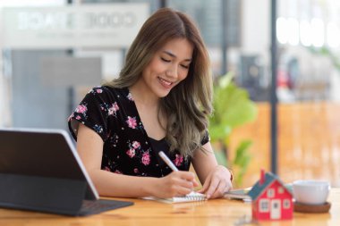 Bayan emlakçı ofis masasındaki not defterine liste yapıyor. Not defterindeki inşaat ücretlerini hesaplayan mimar.