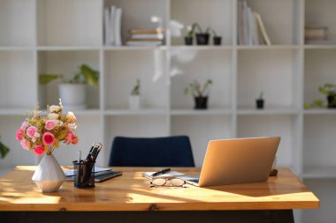 Ahşap ofis masası, siyah ofis koltuğu ve arka planda modern beyaz rafların üzerine dekorasyonlar olan modern bir ofis içi.. 