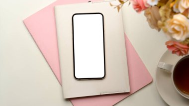 Beyaz arka planda boş akıllı telefon ekran modeli, kitaplar, çiçekler ve çay fincanı olan kadın ofis çalışma alanı.