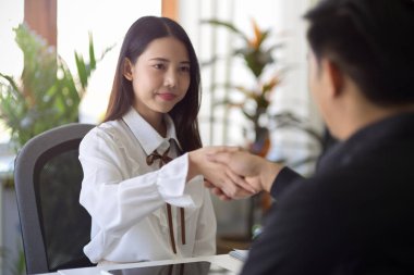 Asyalı kadın yönetici ofiste yeni çalışanın elini sıkıyor. İş görüşmesi, işe alım, tebrikler, anlaşma.