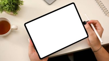 Minimal beyaz ofis masası, yanında taşınabilir tablet taşıyan bir kadın. Stylus kalemle boş ekran modeli. Tasarımcı, çizim, tablet dokunmatik tablet üzerinde çalışma.