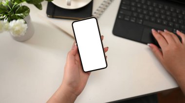 Akıllı telefonlu boş ekran tutan ve masasındaki taşınabilir tablet bilgisayarda çalışan bir kadın işçi..