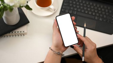 Akıllı telefon beyaz ekran maketi tutan bir kadın eli olan modern ofis çalışma alanı. en üstteki görünüm