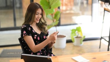 Çekici ve muhteşem Asyalı kadın kafede oturur ve modern akıllı telefonunu kullanır. Teknoloji konsepti olan insanlar