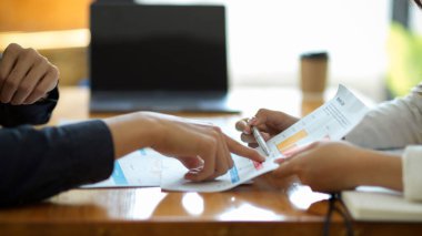 Kesilmiş görüntü, iki iş kadını ofiste mali ve pazarlama verilerini tartışıyor ve analiz ediyor. Kadın, raporu işaret ediyor..