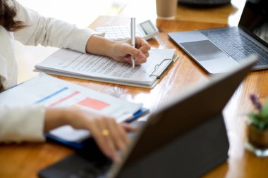 Taşınabilir tablet dokunmatik bilgisayarda çalışan ve ofis masasındaki belge formunu dolduran bir iş kadınının kırpılmış resmi..