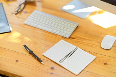 Ofis malzemeleri, kırtasiye malzemeleri, kablosuz klavye, bilgisayar, ahşap masada boş bir spiral defter. yakın plan