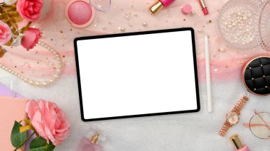 Dijital tablet beyaz ekran modeli, güzellik ürünleri, pembe güller ve pembe aksesuarlı serbest güzellik blogcu çalışma alanı. Üst görünüm, düz uzanma