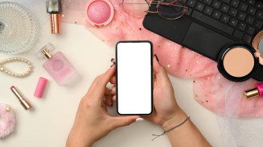 Zarif pembe kadın güzellik blogcusu ya da akıllı telefon beyaz ekran maketi tutan kadın elli makyajcı çalışma alanı. Üst görünüm, düz uzanma