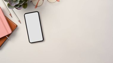 Genel çekim, defter, gözlük, saksı, akıllı telefon beyaz ekran ve beyaz masa arkaplanı üzerine kopyalama alanı olan modern bir çalışma alanı..
