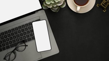Genel çekim, dizüstü bilgisayarı, gözlüğü, kahve fincanı, dekor bitkisi, akıllı telefon beyaz ekran modeli ve siyah arkaplan üzerine kopyalama alanı olan modern ofis masası.