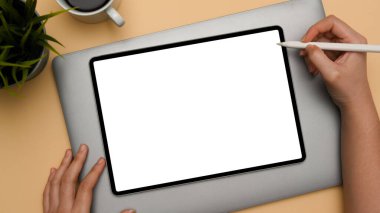 Dijital tablet dokunmatik bilgisayarında bej ofis masası arka planında stilus kalem çizimi yapan bir kadın el. en üstteki görünüm