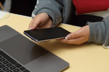 Masasında oturan ve akıllı telefonunu kullanan bir üniversite öğrencisi. yakın plan, telefon siyah ekran