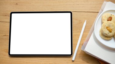 Tepeden çekim, dijital tablet dokunmatik dokunmatik tablet beyaz ekran modeli, stilus kalem ve ahşap masada bir tabak kurabiye..