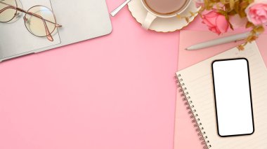 Pembe arka planda fotokopi alanı olan bayan ofis masası, akıllı telefon beyaz ekran modeli ve aksesuarları. en üstteki görünüm