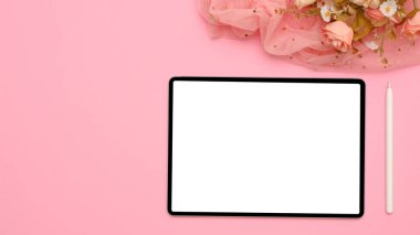 Üst görünüm, düz alan, taşınabilir tablet bilgisayarlı beyaz ekran, stilus kalem, çiçek buketi ve pembe arkaplanda kopyalama alanı.