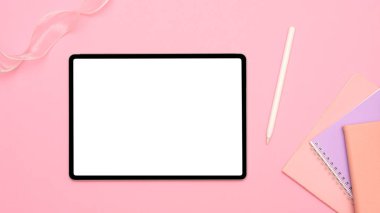 Taşınabilir tablet dokunmatik ekranlı çalışma alanı boş ekran maketi, pembe masa arka planında stilus kalem ve not defterleri. Yukarda, düz yatıyordu
