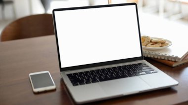 Yakın plan, taşınabilir bir dizüstü bilgisayar beyaz ekran modeli, akıllı telefon, not defterleri, ahşap ofis masasında bir tabak kurabiye. Ofis masası, çalışma masası, uzaktan çalışan kafe masası..