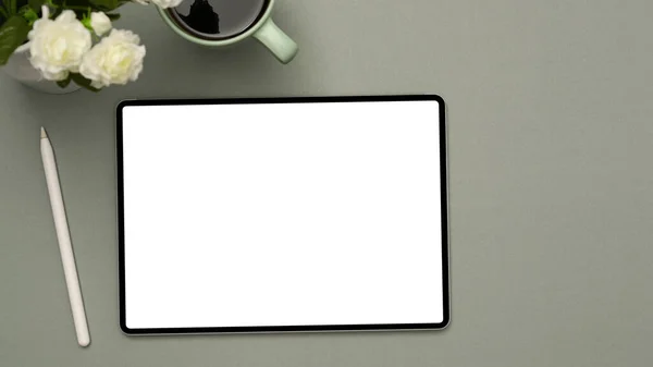 グレーの背景にデジタルタブレットタッチパッドホワイトスクリーンモックアップ スタイラスペン コーヒーカップや花と最小限のオフィステーブルの背景 トップビュー — ストック写真