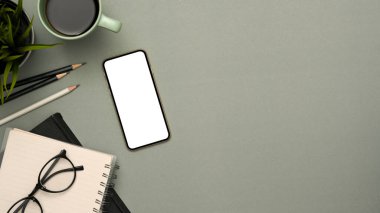 Üst görünüm, ürün gösterimi için kopya alanı olan gri arkaplan, akıllı telefon beyaz ekran, kahve fincanı, gözlük ve kırtasiye malzemesi.