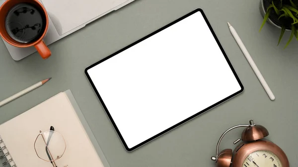 ノートパッド メガネ コーヒーカップ スタイラスペン ラップトップ ヴィンテージクロック タブレットホワイトスクリーンモックアップを備えたモダンなワークスペースは グレーの背景に画面にグラフィックを表示します トップビュー — ストック写真