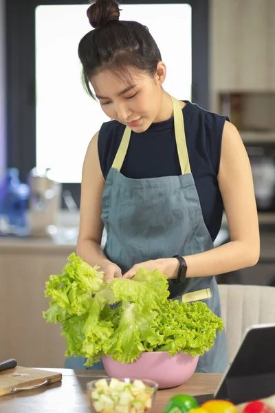 美しいですアジアの女性の肖像とともにエプロン彼女の緑野菜のために彼女の健康的なサラダボウルキッチン — ストック写真