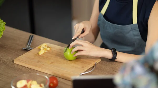 クローズアップイメージでは エプロン付きの女性がキッチンで食べ物を準備していて 木製のまな板に緑のリンゴを切っています 健康的なライフスタイル — ストック写真