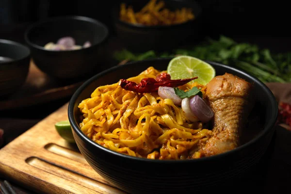 Khao Soi Kai, Northern Thai coconut yellow curry soup with chicken and egg noodles top with coriander, lime, shallots and ground chillies fried in oil.