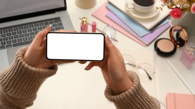 Yakın plan, beyaz ekranlı akıllı bir telefon tutan kadın ofis masasının üzerinde yatay pozisyonlarda..