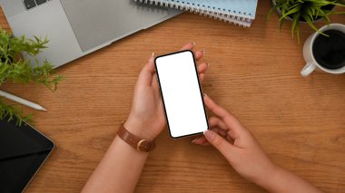 Yakın çekim, üst manzara, kadınların elindeki akıllı telefonun maket ekranı ahşap çalışma masası arka planı..
