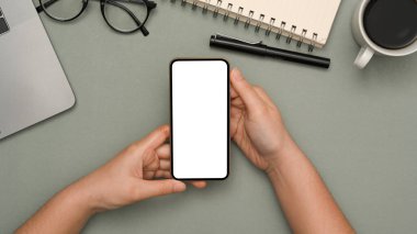 Yakın çekim, üst görünüm, akıllı telefon beyaz ekran masayı tutan kadın eli modern gri ofis çalışma masasında..